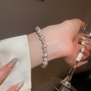 Close-up of elegant pearl bracelet with crystal spheres on woman's wrist holding glass
