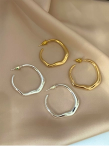 Close-up of irregular twisted hoop earrings in gold and silver on beige silk fabric