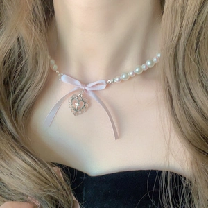 Close-up of pearl necklace featuring a pink silk bow and silver hollow heart cross charm