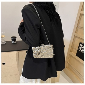 Detail of silver evening clutch bag with lava texture on a black suit and chain strap