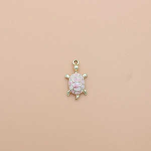 Macro detail of pink enamel turtle charm with golden alloy base on pink background