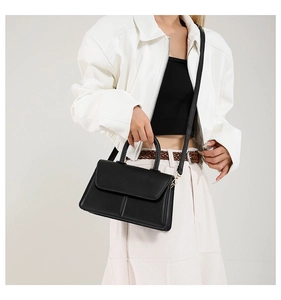 Detail of a structured black leather handbag with top handle and detachable strap