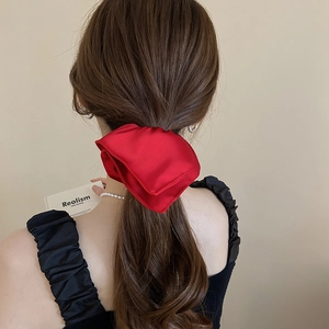Detail of a large red satin bow scrunchie on a brunette ponytail for a stylish look