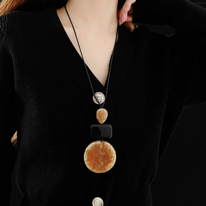 Detail of amber water-drop and round resin pendants on a vintage long sweater necklace