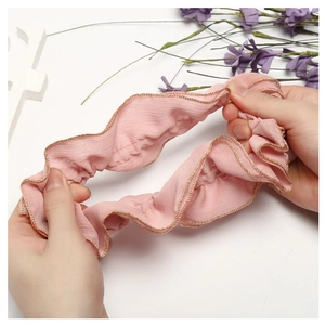 Pink fabric hair scrunchie with gold trim being stretched to show elasticity