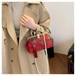 Close-up of a red vintage handbag with floral print, pearl chain and a silk tassel