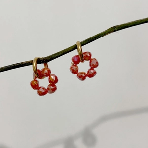 Detailed view of red crystal flower pendant earrings hanging on a rustic wooden branch