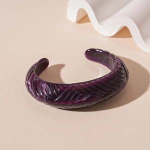 Detail of a deep purple acrylic cuff bracelet with marble texture and grooved relief