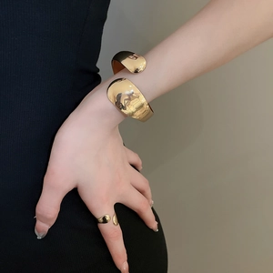 Close-up of a wide polished gold open bangle and matching ring worn by a model
