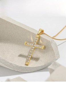 Close-up of golden cross pendant with sparkling zircons on textured stone base