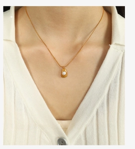 Detail of gold thin chain necklace with irregular frame and white pearl on model