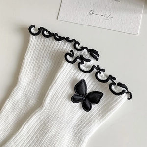 Close-up of white ribbed socks with black wave lace trim and a 3D bow accent