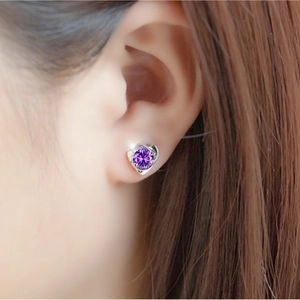 Detail view of heart-shaped silver stud earring with a round purple gemstone on a model