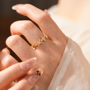 Close-up of a gold ring featuring three pink and clear zircon butterflies on a model's finger