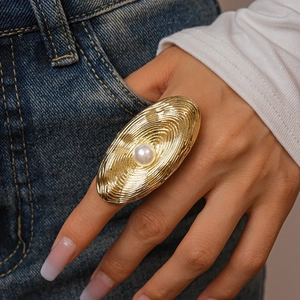 Detailed close-up of a golden oval spiral textured ring with a white center pearl