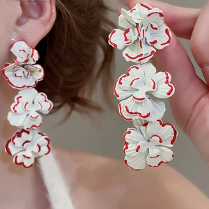 Close-up of three-tier white floral drop earrings with red edge detailing on a model
