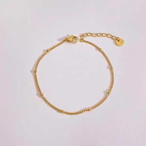 Nahaufnahme von minimalistischem Gold-Edelstahl-Perlenarmband auf hellrosa Grund