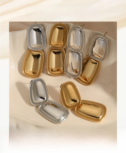 Detail von quadratischen geometrischen Ohrsteckern in Gold und Silber auf einer Keramikschale