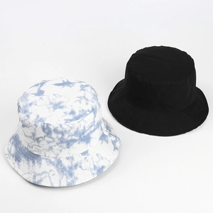 Flat lay of a black bucket hat next to a blue and white tie-dye sun hat on white background