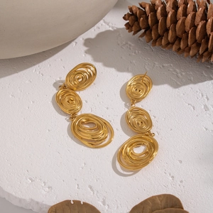 Macro detail of gold-plated swirling tassel earrings on white stone surface