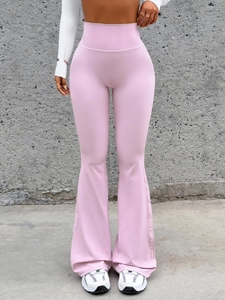 Full view of pink high-waisted flared yoga pants on a model against a concrete wall