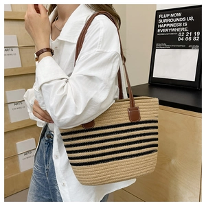 Dettaglio della borsa tote in paglia intrecciata con strisce nere e manici in pelle marrone