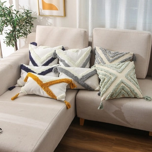 Close-up of tufted geometric cushion covers with fringe tassels on a beige sofa