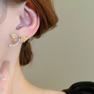 Detail view of dragonfly earrings with yellow crystals and cubic zirconia worn by model