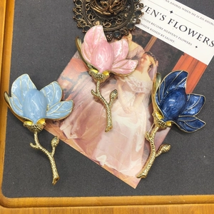 Detailed view of three magnolia flower brooches in pink, light blue, and dark blue enamel