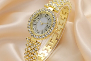 Close-up of golden fashion watch with rhinestones on dial and band over silk background
