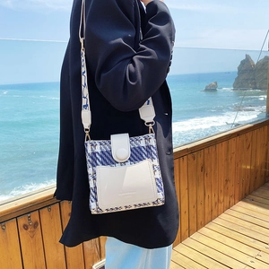 Elegant tweed crossbody bucket bag with wide strap on a seaside wooden terrace background