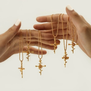 Close-up of five golden necklaces featuring birth flower cross pendants held in hands