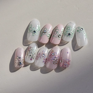 Détail de faux ongles roses et blancs avec motifs floraux métalliques et petits strass