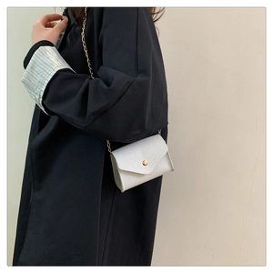 Detail of white crocodile texture mini bag with golden chain strap on a model