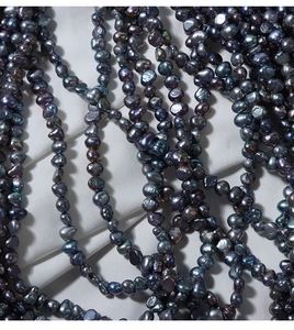 Macro view of peacock green and purple baroque freshwater pearls on white silk