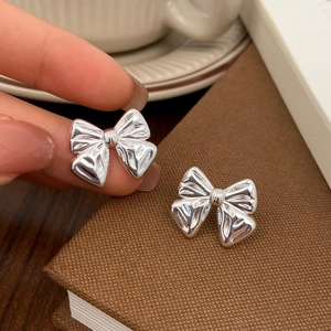 Macro shot of polished silver bow stud earrings held between fingers with glossy finish