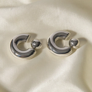 Detail of silver C-shaped steel earrings with ball ends on smooth silk background