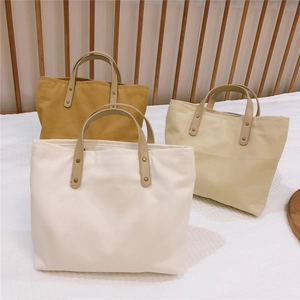 Detailed view of canvas tote bags in white, beige and yellow with leather handles