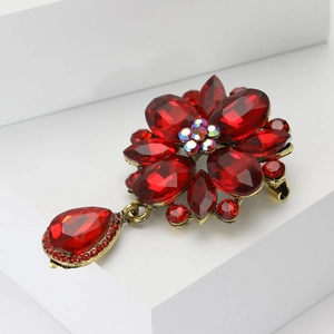Vintage floral brooch with deep red gemstones and gold finish on a white pedestal