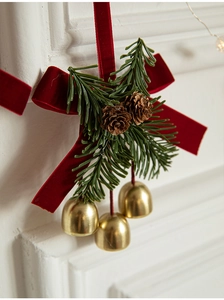 Close-up of red velvet bow with green pine needles, pine cones and gold bells