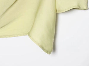 Macro shot of light green fabric texture and fine stitching on asymmetric shoulder top