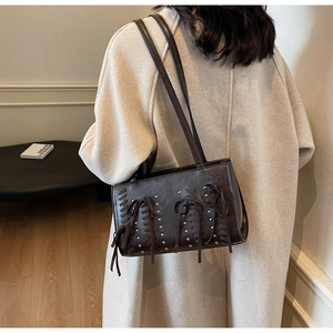 Detail of dark brown faux leather bag featuring woven cord, fringe knot and metal rivets