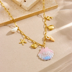 Gold-plated ocean theme necklace with pink shell and starfish charms on a sandy beach