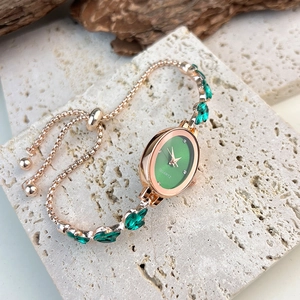 Detail of rose gold quartz watch with green dial and gemstone bracelet strap on stone