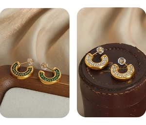 Macro detail of C-shaped gold plated earrings with green and white inlaid crystals