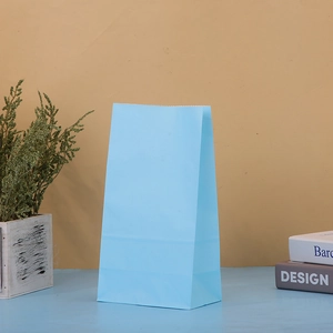 Detail view of a sky blue kraft paper gift bag with serrated edges on a blue desk
