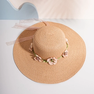 Detail of hand-woven straw sun hat with floral wreath and pink organza ribbon