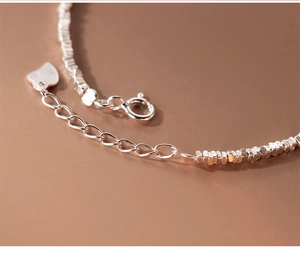 Macro shot of a minimalist silver beaded bracelet with heart pendant and lobster clasp