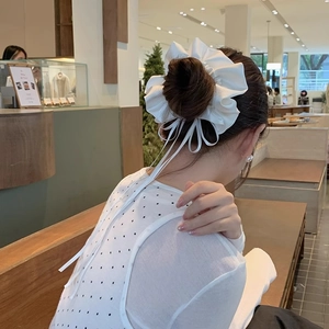 White satin bow hair scrunchie with long ribbons worn on a bun hairstyle for women