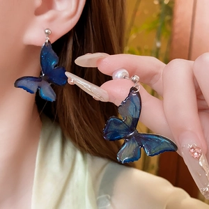 Close-up of blue butterfly earrings with white pearl and gradient glitter texture